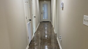 A hallway with a marble floor, white walls, and doors leading to rooms.