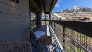 A balcony with wicker chairs and a patterned rug, overlooking a mountainous landscape. - Wood Creek Condo | 2 Bedroom | Shared Hot Tub | Mtn Vew | Balcony | Parking (Mt. Crested Butte)