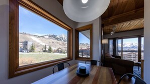 A dining area with a wooden table and chairs, large windows with a mountain view, and a ceiling light fixture. - Wood Creek Condo | 2 Bedroom | Shared Hot Tub | Mtn Vew | Balcony | Parking (Mt. Crested Butte)