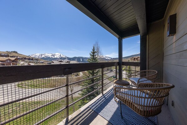 A balcony with wicker furniture, a patterned floor, and a view of snow-capped mountains.