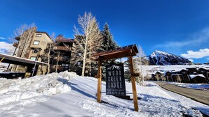 A snow-covered lodge entrance with a sign indicating 'Wood Creek Lodge' at Mt. Crested Butte, 400 Gothic Rd. - Wood Creek Condo | 2 Bedroom | Shared Hot Tub | Mtn Vew | Balcony | Parking (Mt. Crested Butte)