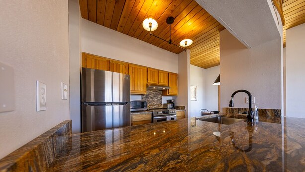 A modern kitchen with a granite countertop, stainless steel appliances, wooden cabinets, and a wooden ceiling. - Wood Creek Condo | 2 Bedroom | Shared Hot Tub | Mtn Vew | Balcony | Parking (Mt. Crested Butte)