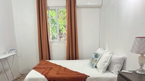 Ein ordentlich bezogenes Bett mit einem gemusterten Überwurf und einer braunen Tagesdecke, eine Nachttischlampe und ein Fenster mit Vorhängen.