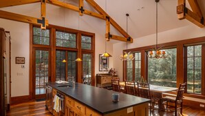 A spacious kitchen with a large island, wooden beams, and large windows offering views of the outdoors.