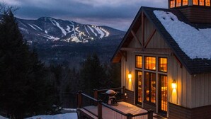 A wooden cabin with a snow-covered roof, large windows, and a deck with a stroller.