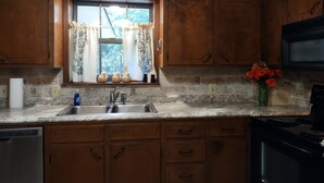 Una cucina con mobili in legno, un piano di lavoro in granito, un lavello in acciaio inossidabile e un fornello.
