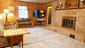 Un soggiorno con camino, pareti in legno, un divano, una televisione e un gioco da tavolo.