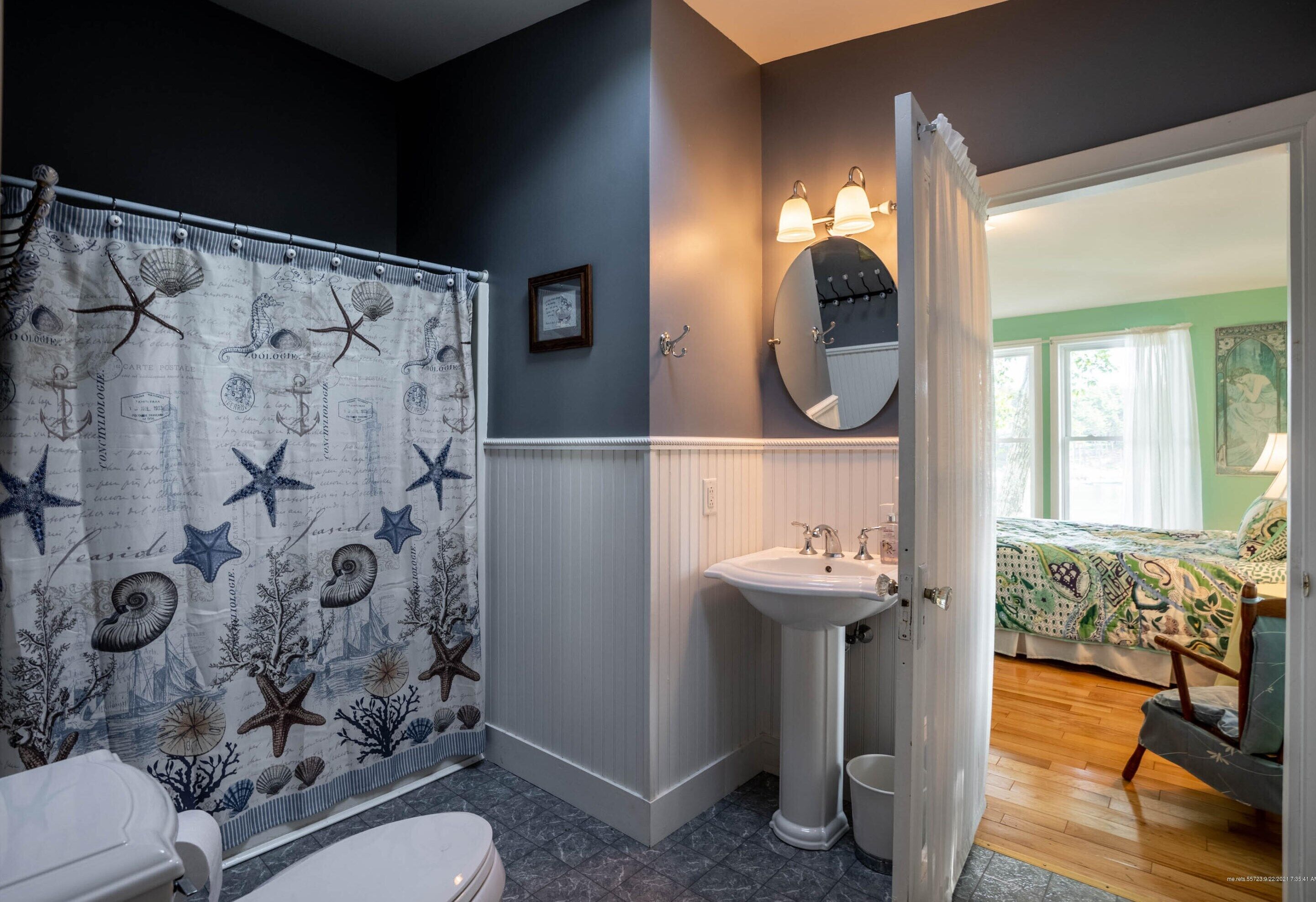 Une salle de bain avec un rideau de douche orné de motifs marins, un lavabo sur pied et un miroir au-dessus.