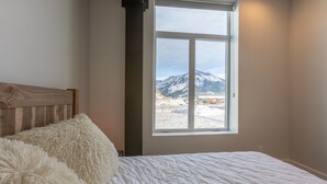 A bedroom with a large window, a wooden headboard, and fluffy white bedding.