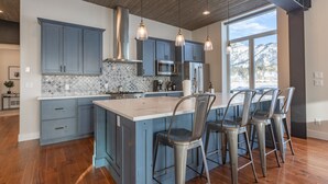 A modern kitchen with blue cabinets, a large island, stainless steel appliances, and bar stools.