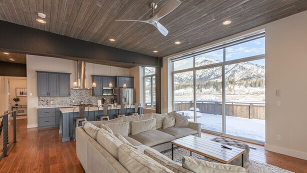 A spacious living area with a large sectional sofa, a wooden coffee table, and a view of a snowy landscape through large windows.