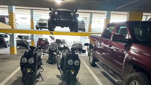 Un aparcamiento de varios niveles con varias motocicletas y un SUV color borgoña estacionados.