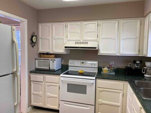 A kitchen with white cabinets, a microwave, an oven, and a sink.