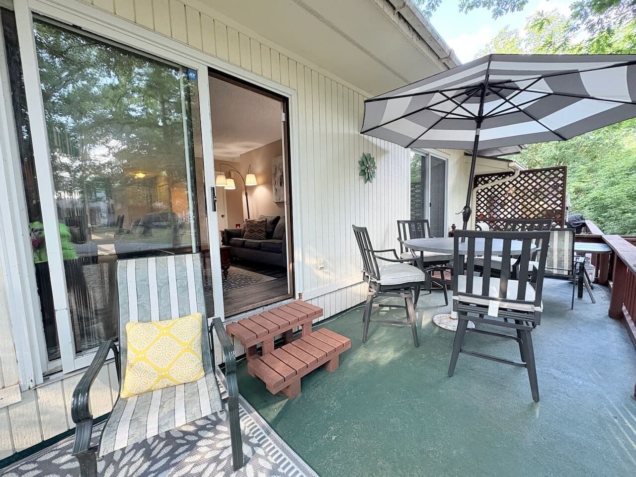 Un patio techado con mobiliario exterior, una puerta corrediza de vidrio que da a un espacio interior y una terraza de madera.