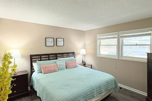 A bedroom with a bed, two bedside tables, a window, and wall decorations.