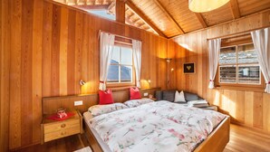 A wooden-paneled bedroom with a large bed, two bedside tables, a nightstand, and a window with curtains.
