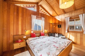 A wooden-paneled bedroom with a large bed, two bedside tables, a nightstand, and a window with curtains.