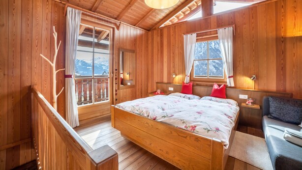 A wooden cabin bedroom with a bed, bedside tables, and a window with a view.