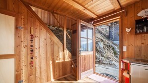 A wooden cabin with a wooden staircase, a door leading outside, and a kitchen area with a refrigerator.