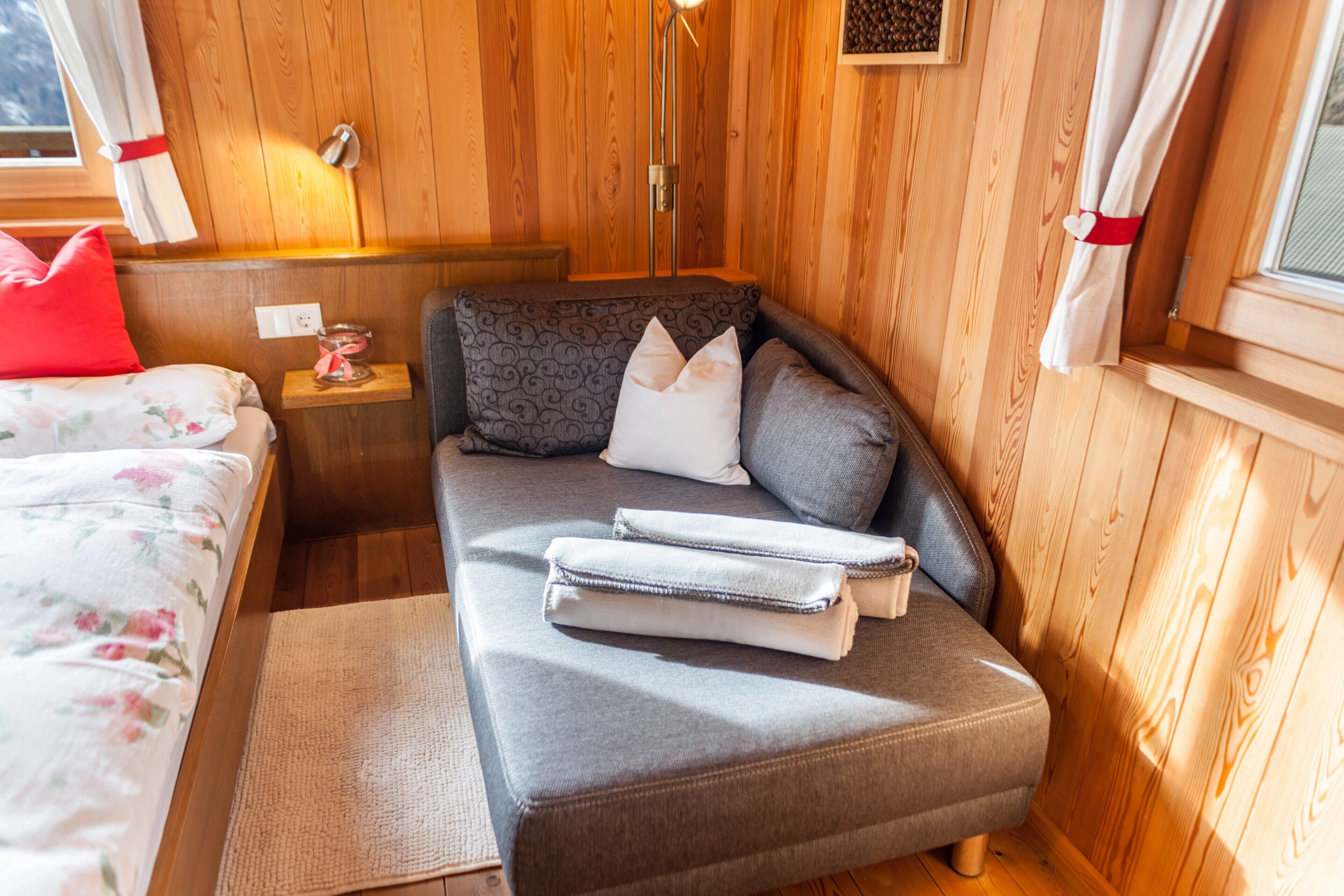 Ein gemütliches Zimmer mit einer Couch, einem kleinen Tisch mit Kerze und einem fenster mit Vorhängen.