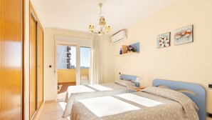 A hotel room with two beds, a chandelier, artwork on the wall, and a view through the window. - Beachfront Penthouse with Wi-fi & Pool (San Javier, Murcia)