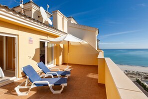 Un balcon avec des chaises longues, un parasol blanc et une vue sur la mer.