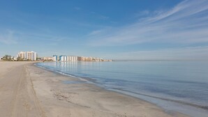 A beach with a calm sea, a sandy shore, and a row of buildings in the background. - Beachfront Penthouse with Wi-fi & Pool (San Javier, Murcia)