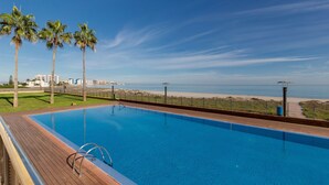 A swimming pool with a wooden deck, palm trees, and a view of the beach and ocean. - Beachfront Penthouse with Wi-fi & Pool (San Javier, Murcia)