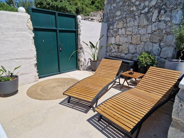 A sunlit outdoor seating area with two wooden lounge chairs and a small table, surrounded by potted plants and a stone wall. - Cozy Coastal Retreat in Dubravica (Dubravica)