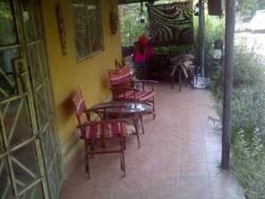 Un patio cubierto con sillas y una mesa de madera, rodeado de paredes amarillas y suelo de baldosas.