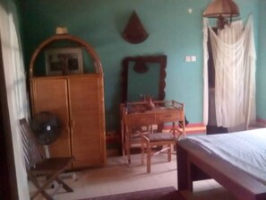 Una habitación con una cama, un escritorio de madera, un armario y un ventilador.
