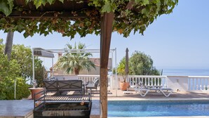 A poolside area with a grill, lounge chairs, and a pergola with vines.