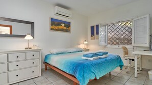 A bedroom with a bed, bedside tables, a desk, a chair, and an air conditioning unit.