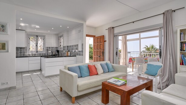 A modern kitchen with white cabinets and a dining area with a white sofa and a wooden table.