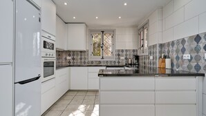 A modern kitchen with white cabinetry, a built-in oven, a window with a view, and patterned backsplash tiles.