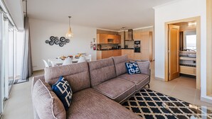 A modern living room with a sofa, a dining table, and a kitchen in the background. - Apartment 'Beachfront Atlantic View A09' with Sea View and Wi-Fi (Óbidos)