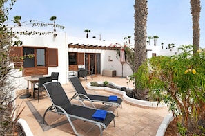 Eine Terrasse mit zwei Lounge-Stühlen, einem Tisch und einem kleinen Gartenbereich mit Pflanzen und einer Palme.