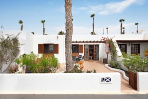 A white building with a patio area, palm trees, and a sign with 'MX' on it.