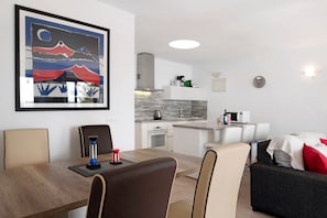 A modern living room with a dining table, chairs, a sofa, and a kitchen in the background.