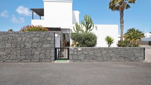 A modern building with a stone wall entrance, a palm tree, and a cactus. - 'Casa Hibiscus' with Private Pool, Jacuzzi, Terrace & Garden (Playa Blanca)