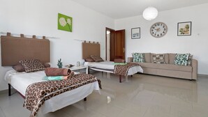 A room with two beds, a sofa, a wall clock, and a green floral painting. - 'Casa Hibiscus' with Private Pool, Jacuzzi, Terrace & Garden (Playa Blanca)