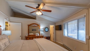 Un dormitorio con cama, ventilador de techo, cómoda, espejo y ventana con persianas.
