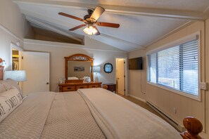 Een slaapkamer met een bed, een plafondventilator, een dressoir, een spiegel en een raam met jaloezieën.