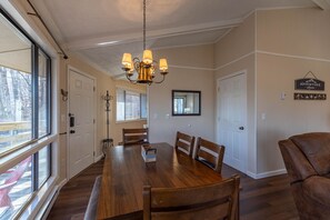 Een eetruimte met een houten tafel, stoelen, een kroonluchter en een uitzicht door grote ramen.
