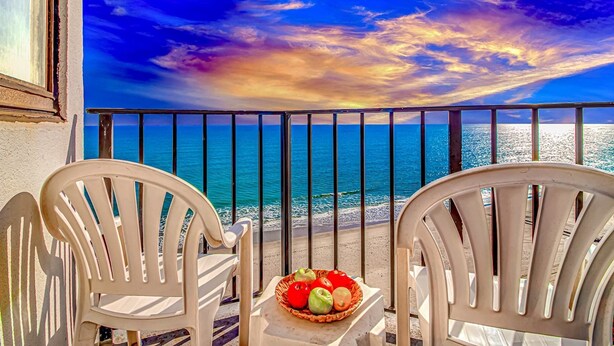 Ein Balkon mit zwei weißen Stühlen und einem Tisch, auf dem eine Fruchtkorb steht.