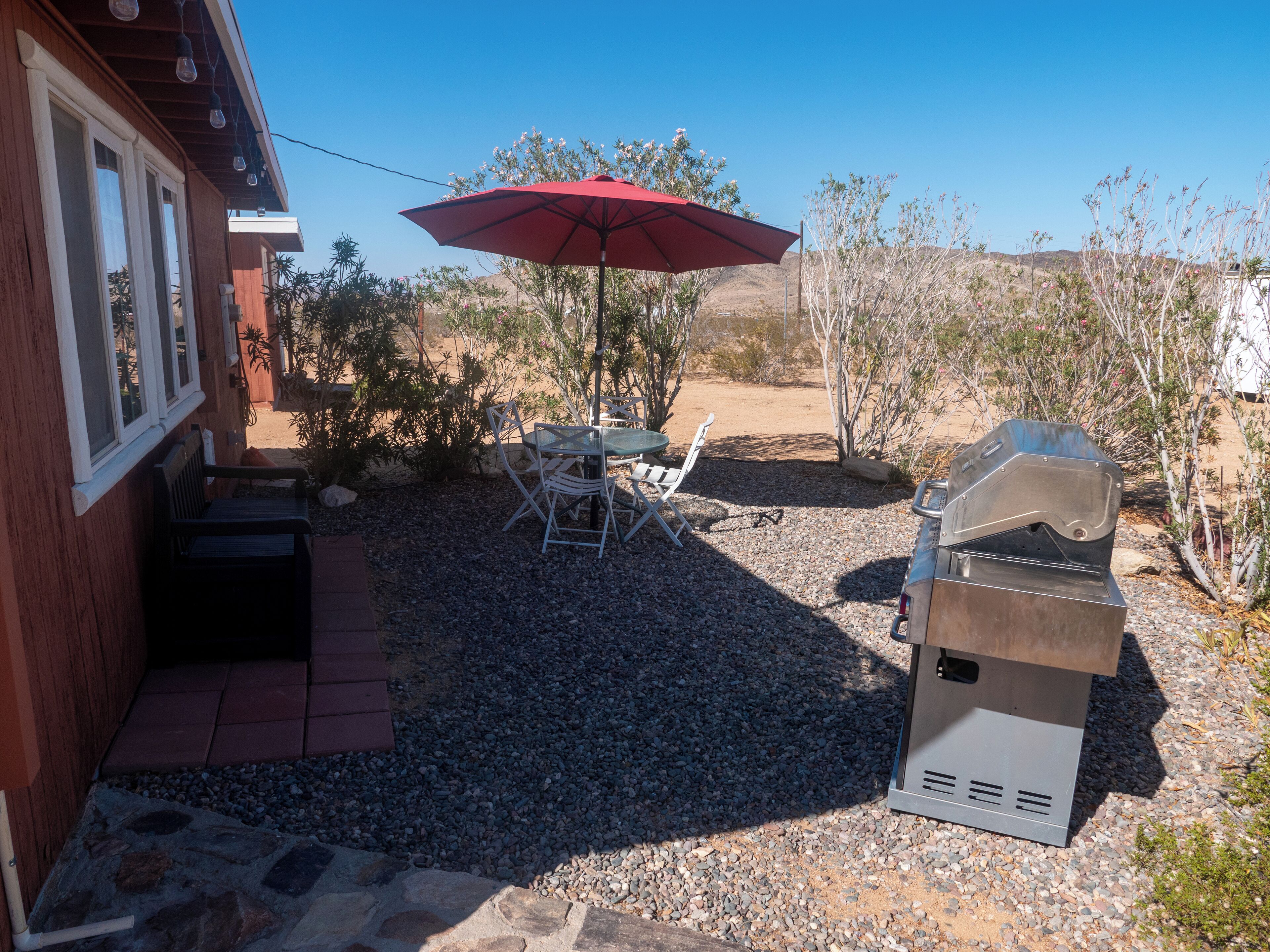 Eine Terrasse im Freien mit Grill, rotem Sonnenschirm und Tisch mit Stühlen.