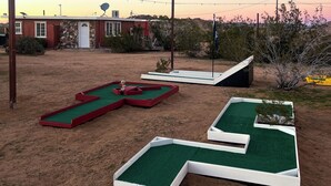 En minigolfbane med flere grønne og røde huller, en stengbygning og en klar himmel.