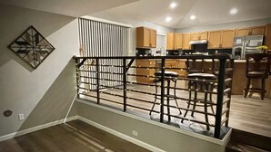Una cocina moderna con armarios de madera, un refrigerador de acero inoxidable y una zona de comedor con taburetes de bar.