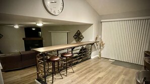 Una cocina con barra de madera y taburetes, un reloj grande en la pared y una puerta corrediza.