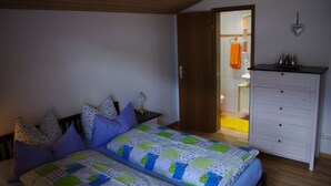 Makuuhuoneessa on sänky, yöpöytä, lipasto ja avoinna oleva ovi, joka johtaa kylpyhuoneeseen.